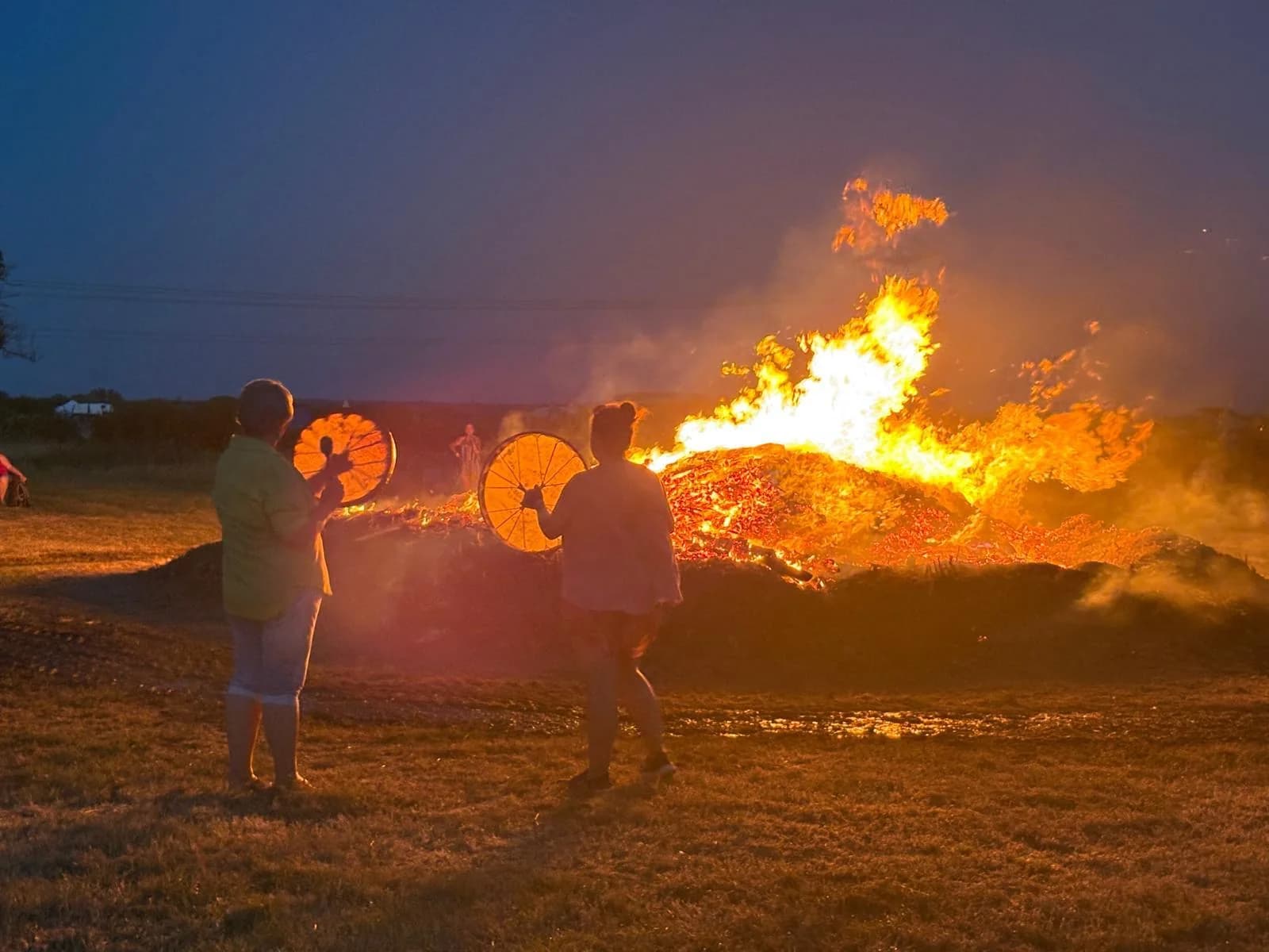 Two campers playing hand drums around the campfire at dusk